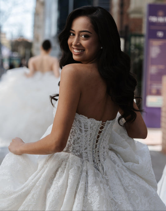 Smiling women in lace SenStudio wedding dress looking over shoulder at camera 