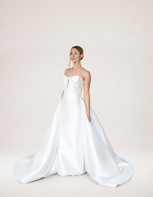 Amira with Keyhole by Aura by Archela - strapless satin sheath with bow detail, keyhole plunge, boned bodice and overskirt with train